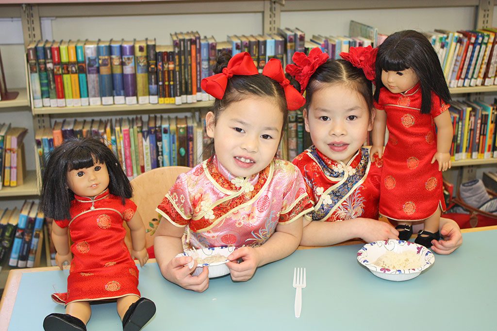 SEVEN-YEAR-OLD twins Lorelei and Annabelle Eckhardt enjoy a bowl of jasmine rice with their dolls during the library’s Chinese New Year Party on Feb. 20. (Dan Tomasello Photo)
