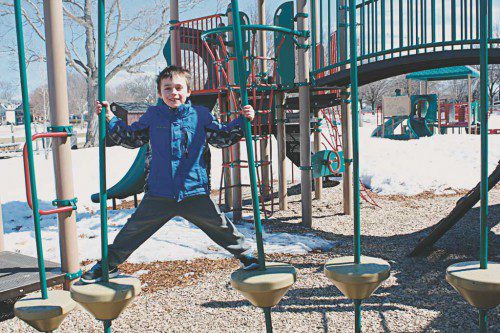 ELIOT BAKER, 6, tests the limits of the floating platform steps on the climbing structure during a visit to the Spaulding Street Playground on April Fools’ Day. (Maureen Doherty Photo) 