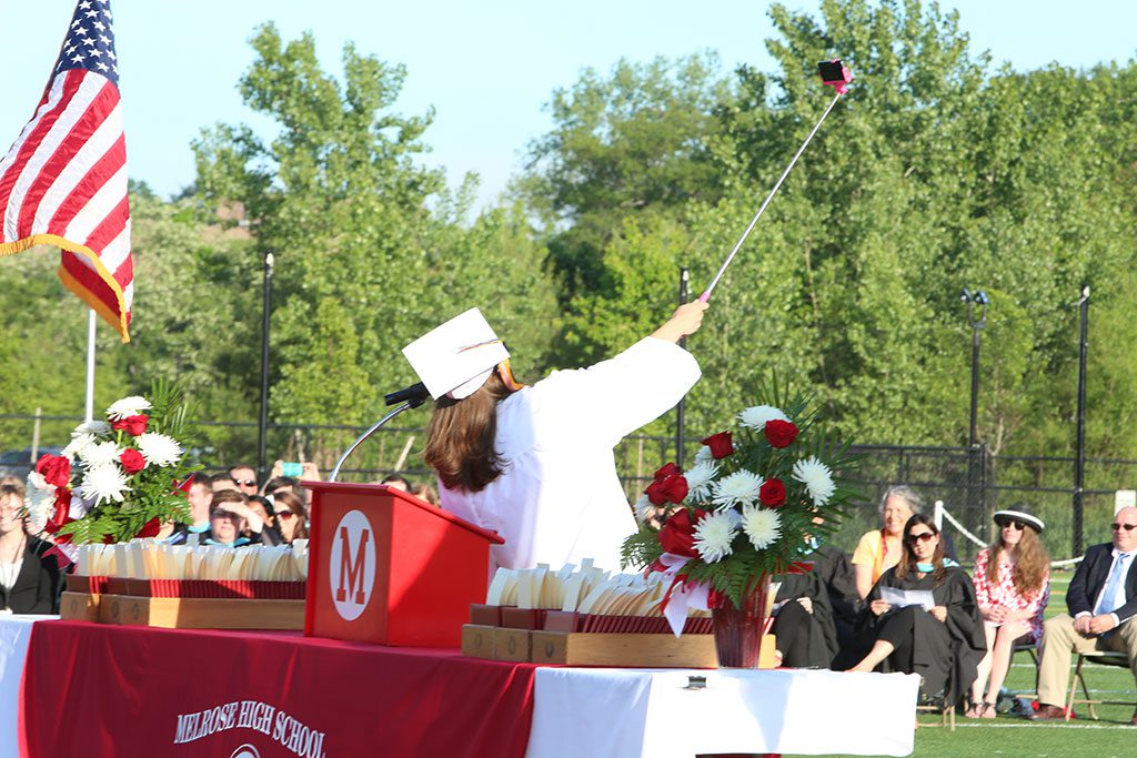 EMILY McCARTHY, who served as Master of Ceremonies during this year’s high school graduation, uses a selfie stick to take a photo of herself and other members of the Class of 2015. (Donna Larsson Photo)