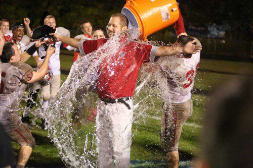 HEAD COACH Steve Cummings (center) gladly gets a Gatorade bucket shower from Zack Kane (#33) as Evan Gourville (#55) takes hold of the coach's electronic equipment. Cummings earned his first victory as head coach with Wakefield's 7-6 triumph over Stoneham on Friday night at Stoneham High School. (Donna Larsson Photo)