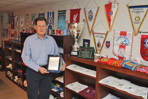 BOSTON BRAVES F.C. President and founder Spiros Tourkakis stands among a small sample of the hundreds of trophies, plaques, team flags and signed memorabilia displayed in his home. The items were exchanged between his soccer team and the nearly 50 international veteran teams the Braves have competed against since 2001. (Maureen Doherty Photo)