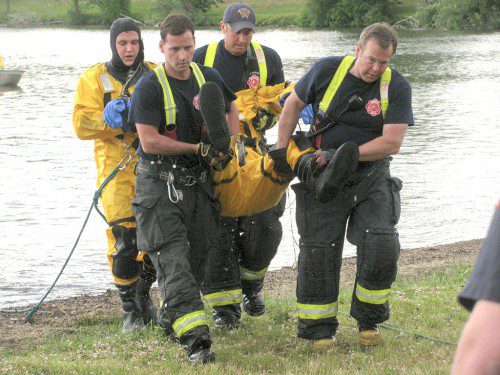 LOCAL FIREFIGHTERS AND EMTs from Action Ambulance carry a “victim” to a waiting stretcher during a simulated drowning rescue at Lake Quannapowitt yesterday. (Mark Sardella Photo)