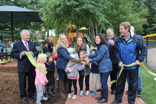 CUTTING the ribbon to celebrate the grand re-opening of Glen Meadow Park last Wednesday were (from left): Selectman Dick Dalton, Erika Wilson, Melissa Adams and Sonia Brady of the Lynnfield Moms Group, Townscape member Richard Sjoberg and Selectmen Chairman Phil Crawford. They were joined by youngsters eager to play on the new playground equipment. (Maureen Doherty Photo)