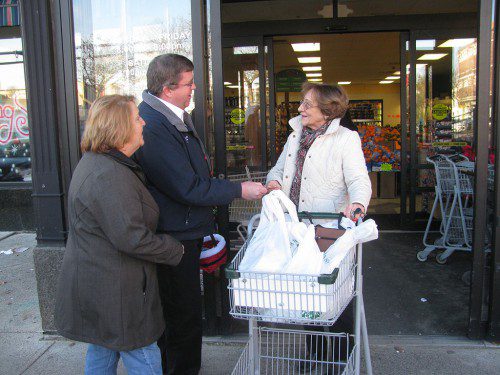 WAKEFIELD CO-OPERATIVE BANK president Mike Wolnick hands a Farmland gift card to customer Lorraine O'Brien yesterday. Bank employees handed 100 gift cards to Farmland customers out in front of the store as a holiday gesture to shoppers in the community. At left is bank employee Jane Coonrod. (Mark Sardella Photo)