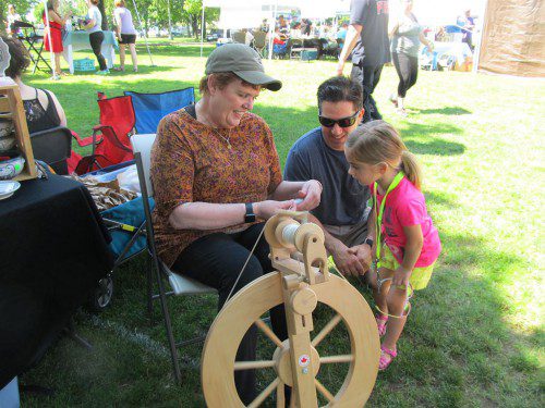 LITTLE ELLA KENT was in awe of Donna Carlstrom of Lynnfield as she spun sheep’s wool at Festival by the Lake on Saturday. Ella was accompanied by her father Jeff Kent of Wakefield.(Gail Lowe Photo)