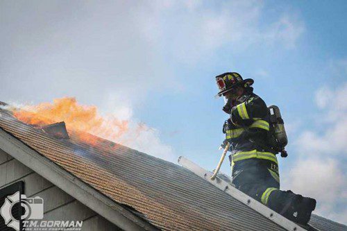 A MEMBER OF THE Melrose ladder company cut a hole in the roof of 62 Goss Ave. Sunday. (Tim Gorman Photo)