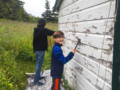 Jackson Shaffer, 13, scrapes paint off a shed in preparation for painting during Aldersgate Methodist Church’s recent mission trip to rural Maine. Read more about their work in this week’s issue of the Transcript. (Courtesy Photo)